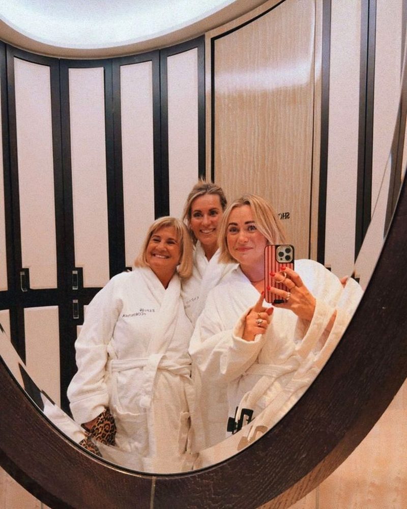Three women in their fifties and sixties in spa robes taking a mirror selfie