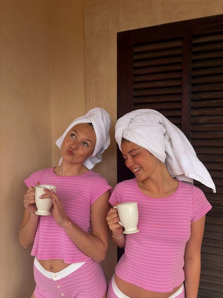 Two friends in pink pyjamas and towel turbans laughing over their morning coffee