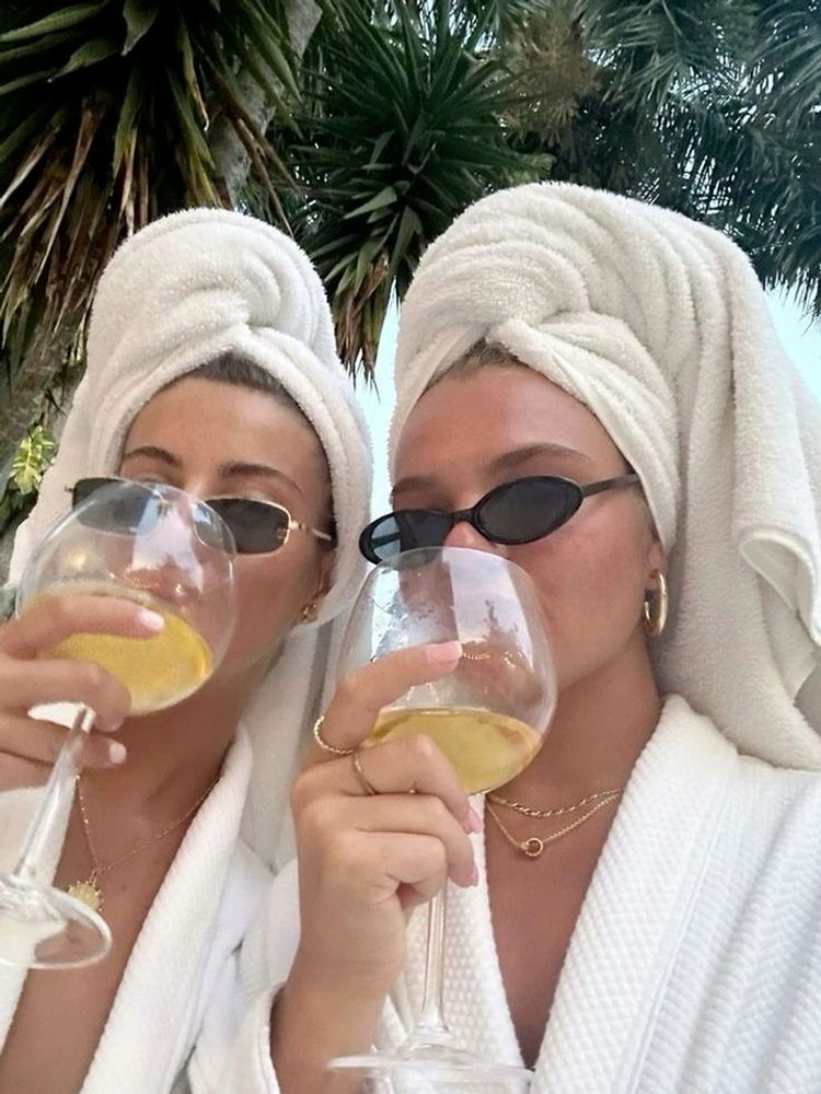 Two friends in robes, towel turbans and tiny sunglasses sipping white wine