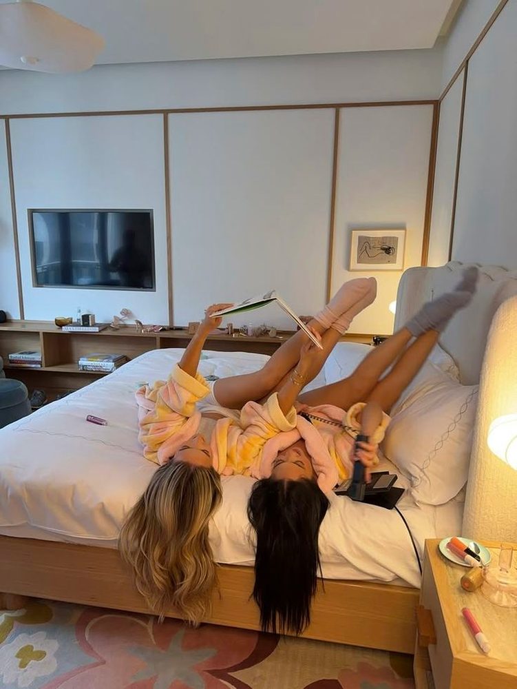 Two friends in fluffy robes lying upside down on a hotel bed with their feet up the wall