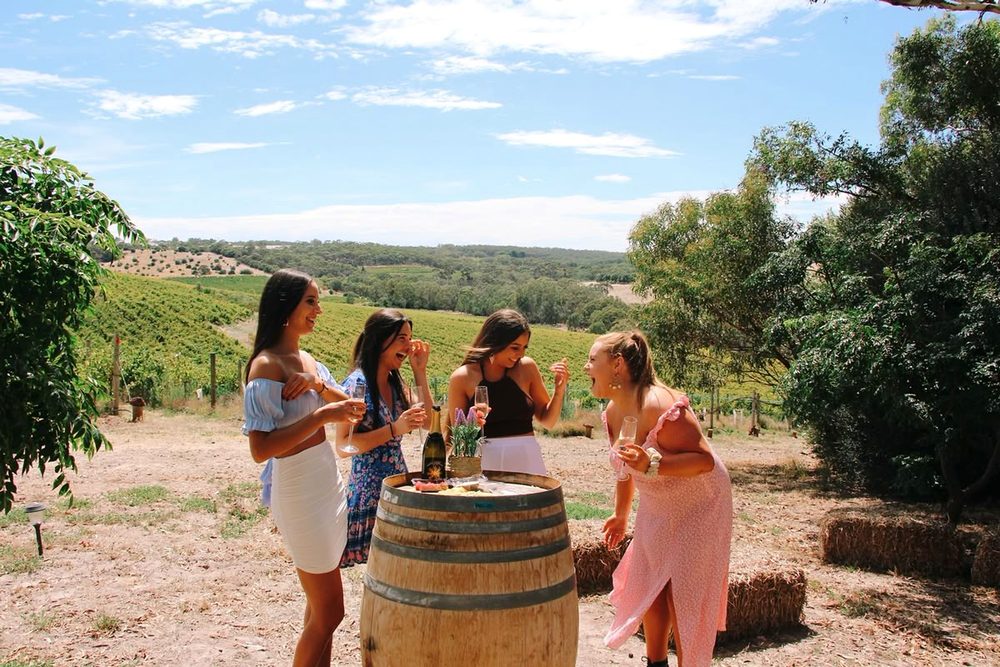 Four friends laughing around a wine barrel with the vineyard rolling away behind them