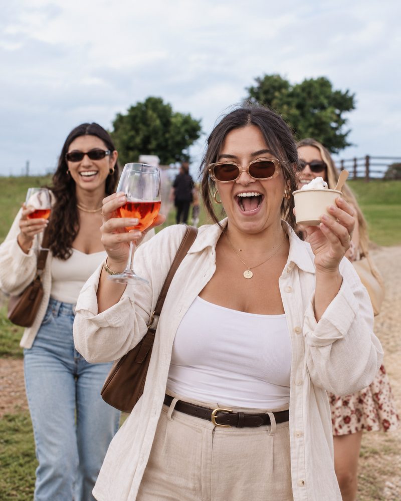 Three friends laughing as they walk across a lawn with rose and soft serve in hand