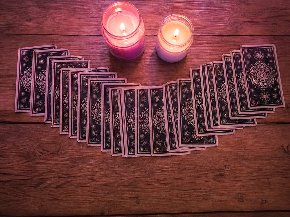 A fan of tarot cards and two candles on a timber table in soft pink light