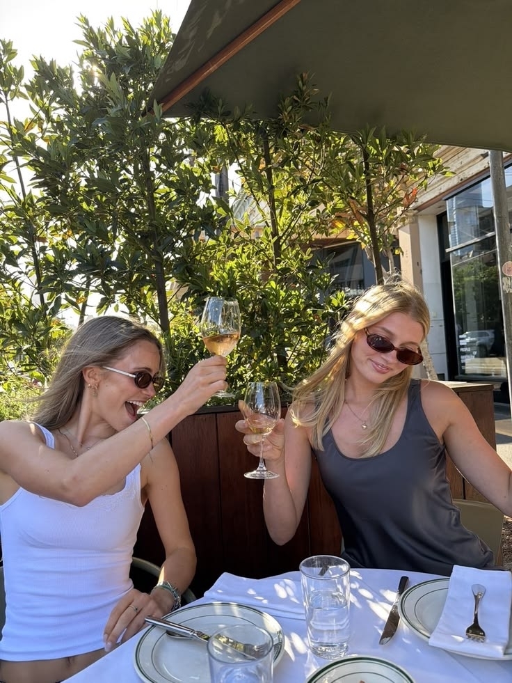 Two friends raising their glasses at a leafy outdoor table