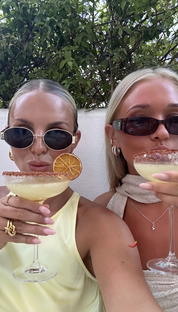 Two friends in sunglasses holding their cocktails up to the camera