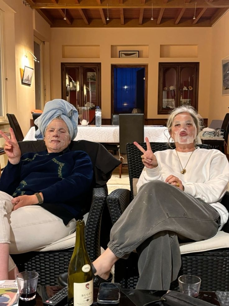Two friends in sheet masks throwing peace signs with a bottle of wine