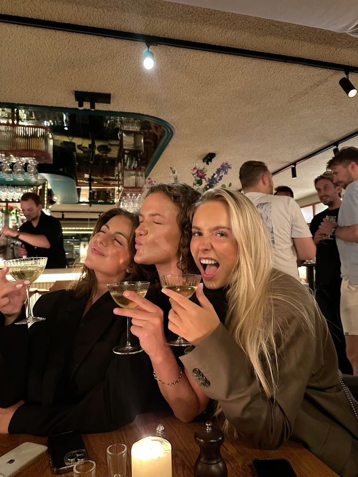 Friends laughing and raising cocktails together at a candlelit bar