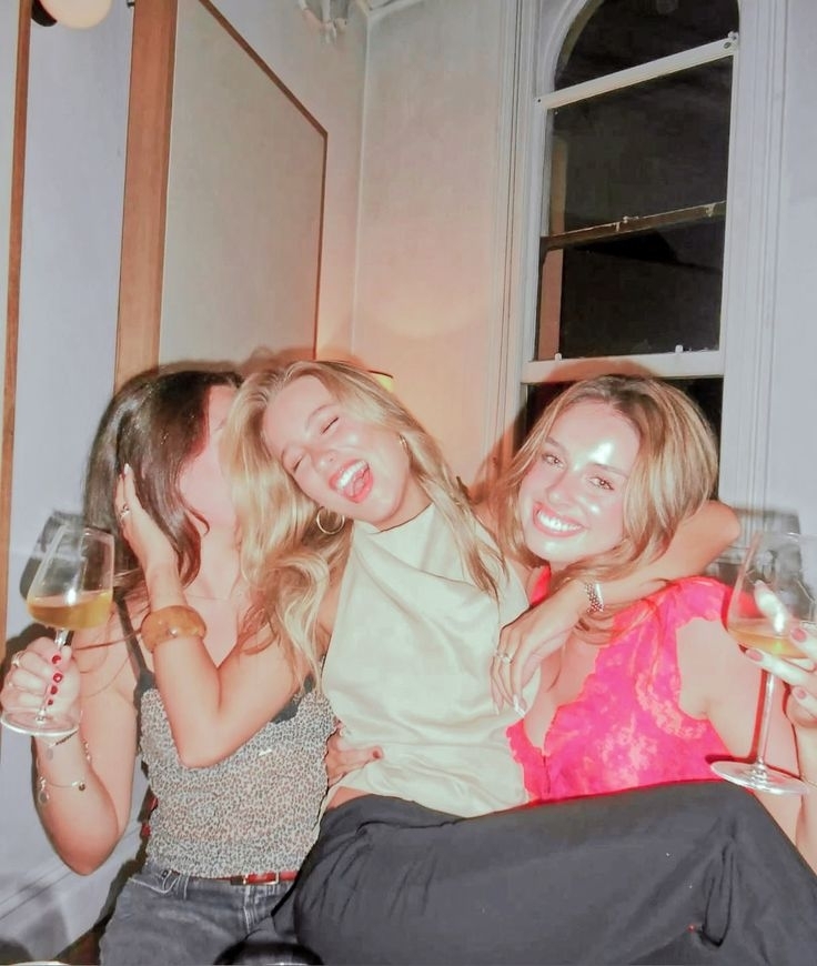 Three friends hugging and laughing with glasses of wine on a girls night in