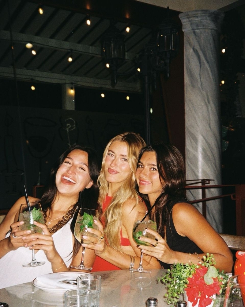 Three friends holding up their cocktails at a lively bar table at night