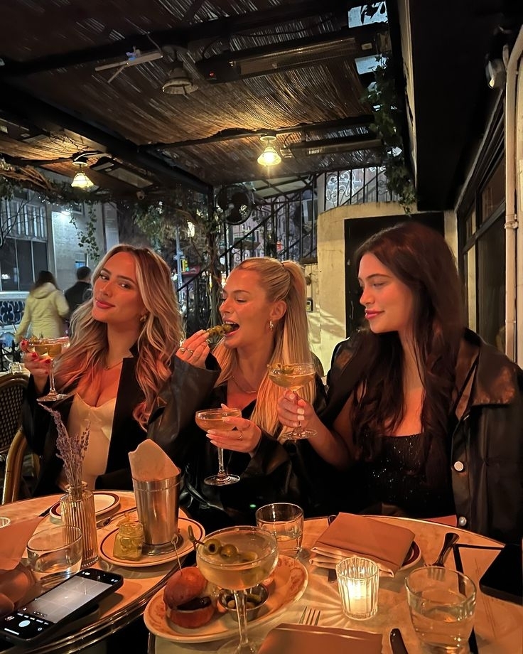 Three friends toasting with cocktails at a candlelit table