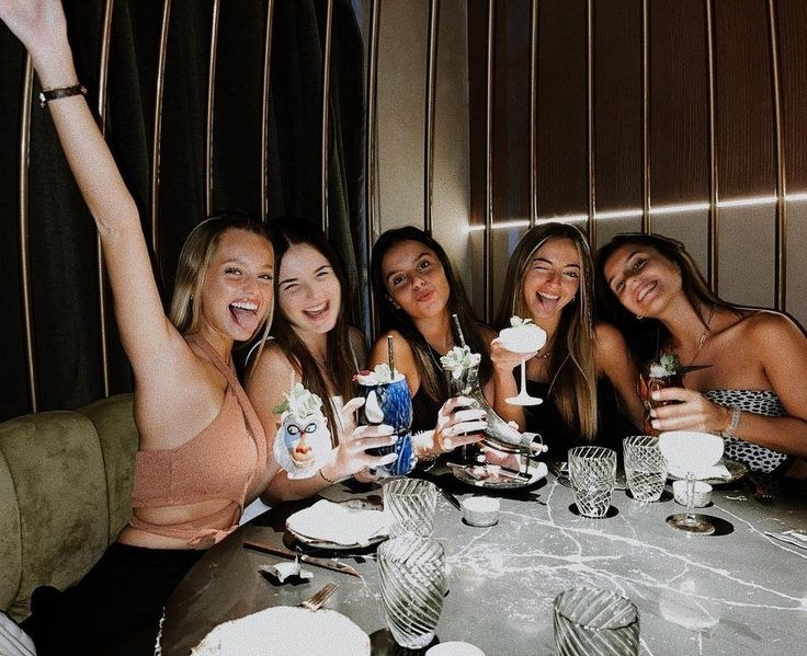 Five friends cheering with cocktails around a marble table on a night out