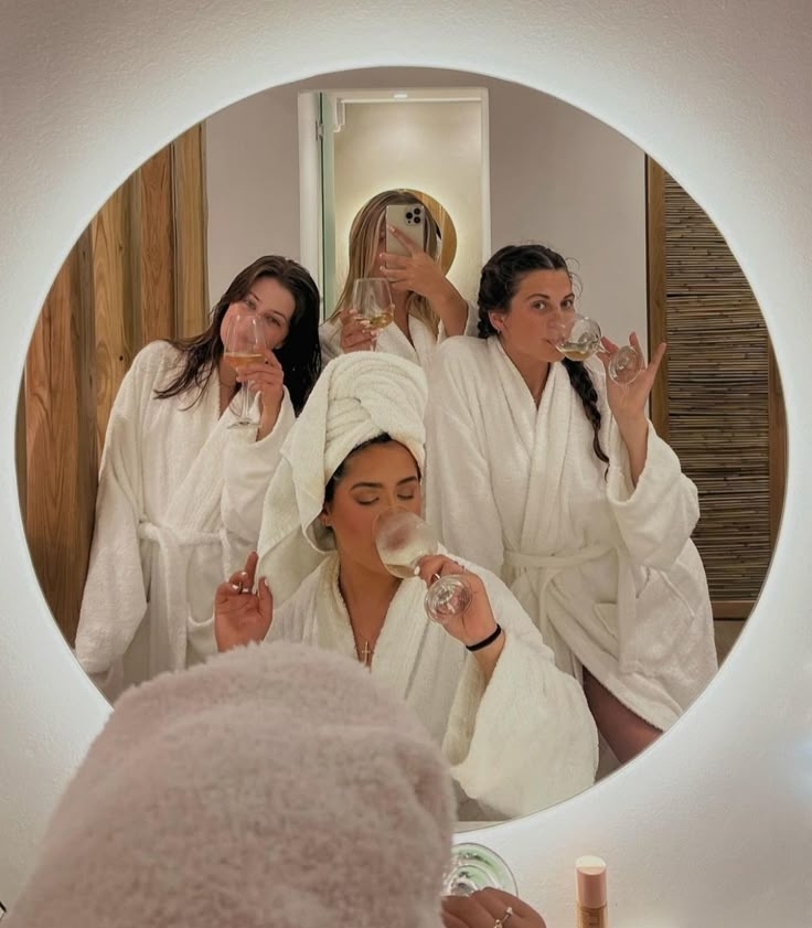 Friends in robes sipping bubbly in a round mirror selfie while getting ready