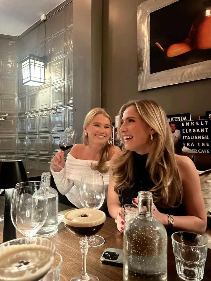 Two friends smiling over espresso martinis and red wine at a restaurant table