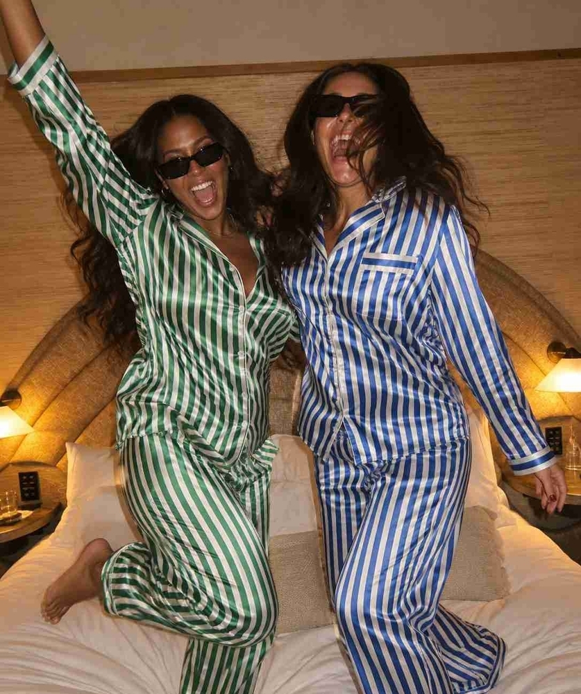 Two friends in silk pyjamas and sunglasses dancing on the bed