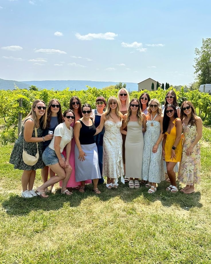 A big group of friends in sundresses posing together in front of the vineyard