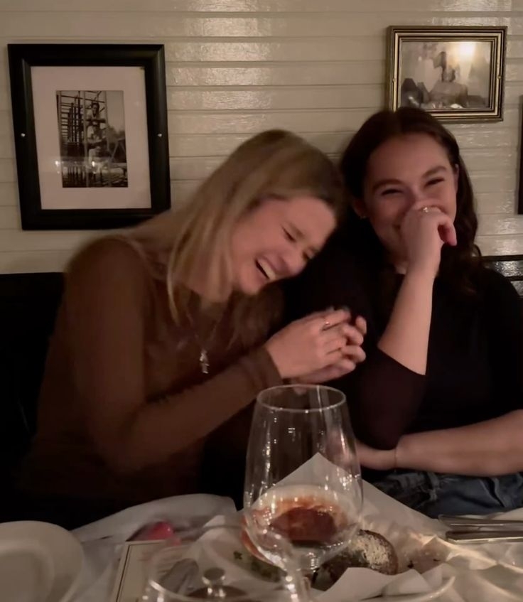 Two friends doubled over laughing at the dinner table