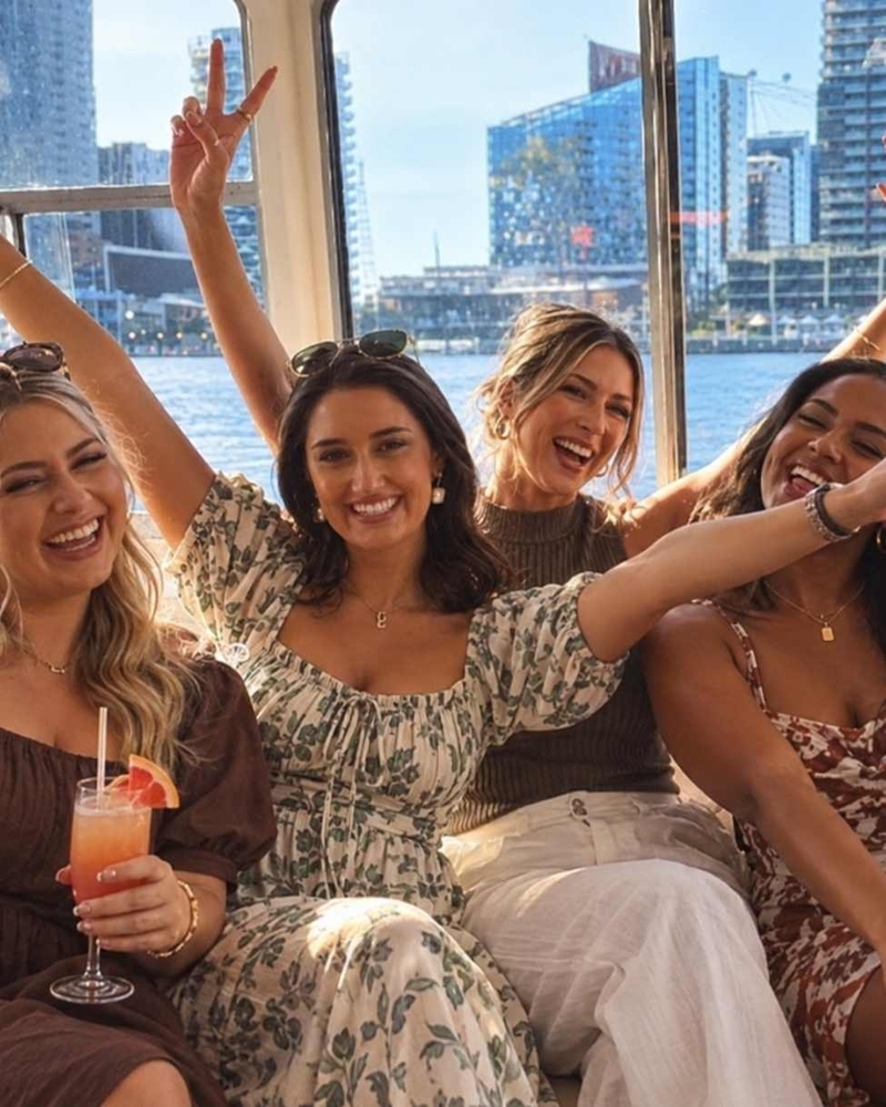 Four friends cheering with cocktails on a boat cruise past the city skyline