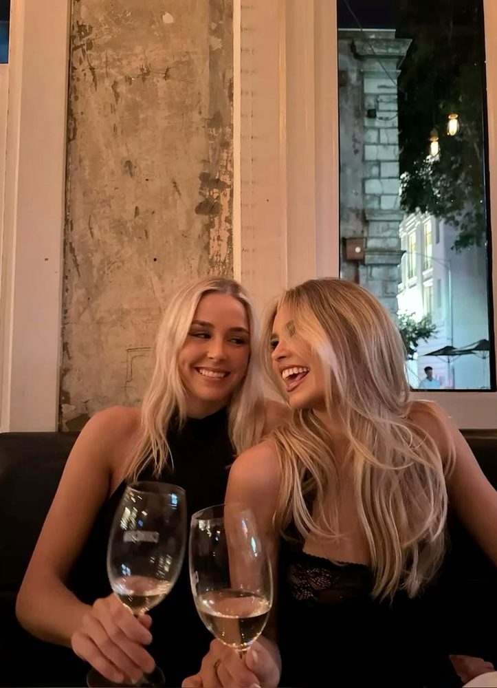 Two friends laughing and clinking white wine in a cosy booth at night