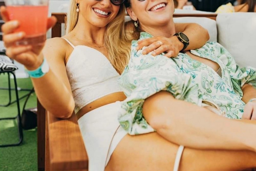 Two friends in sunglasses laughing and toasting on a rooftop