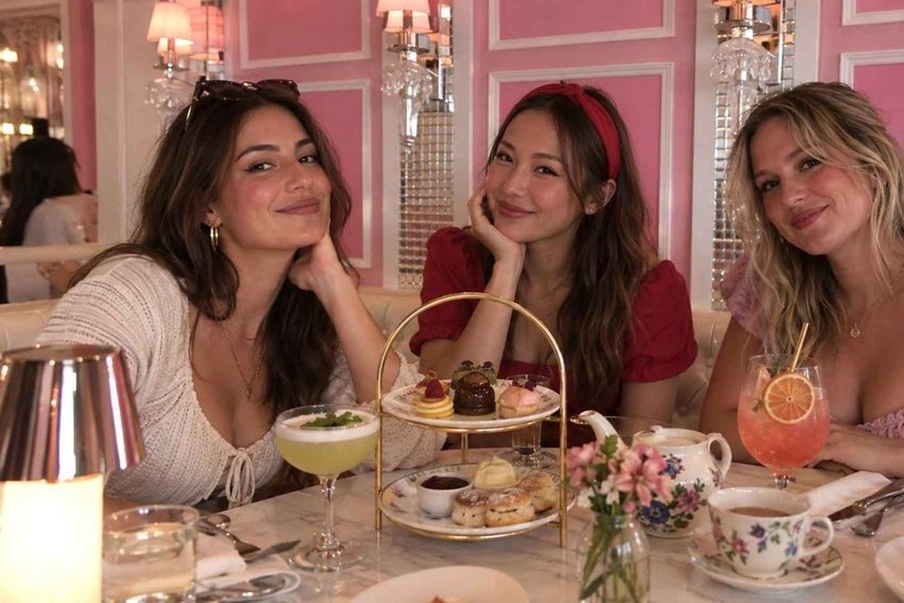 Three friends smiling over a tiered high tea stand and cocktails