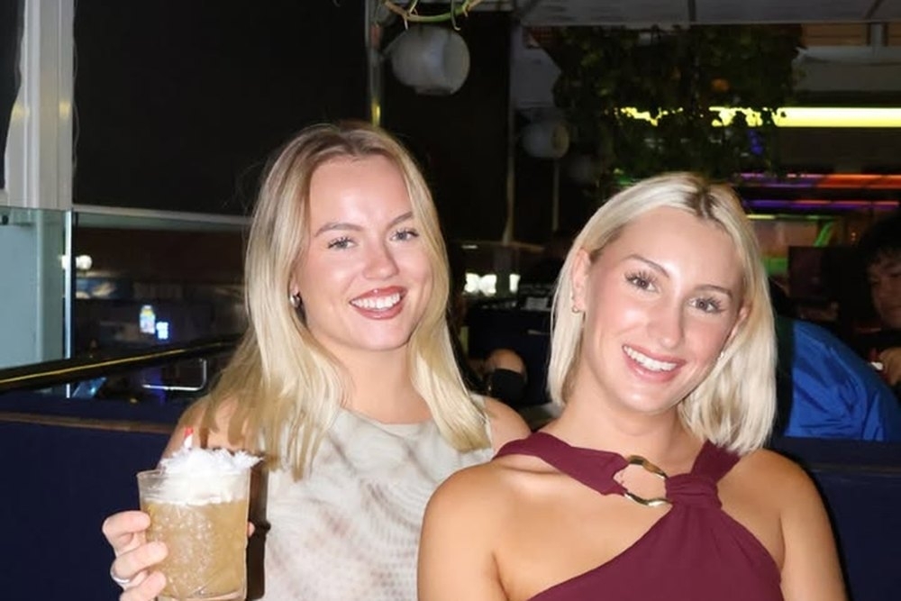 Two friends smiling with drinks at a table on a night out