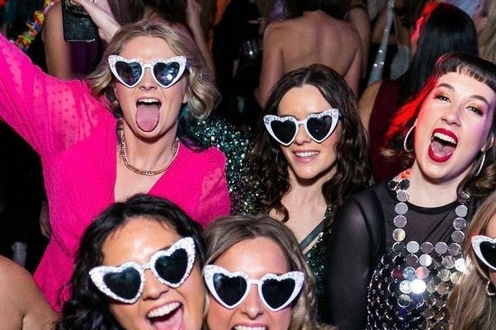 Friends in heart shaped sunglasses screaming with joy in a crowded club