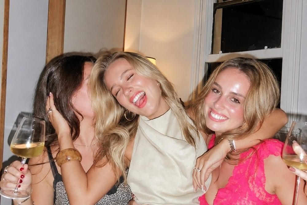 Three friends hugging and laughing with wine in the apartment