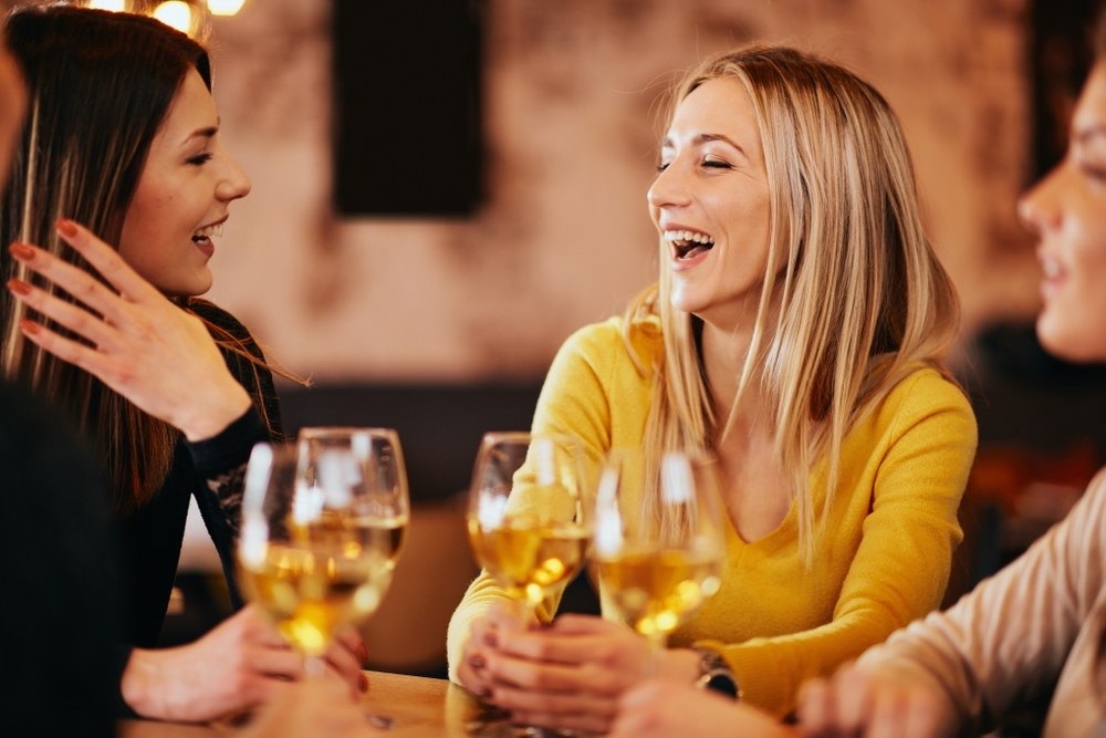 Friends laughing over glasses of sparkling at a cosy wine bar