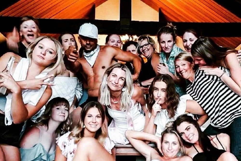 A big group of friends laughing and posing with their topless waiter