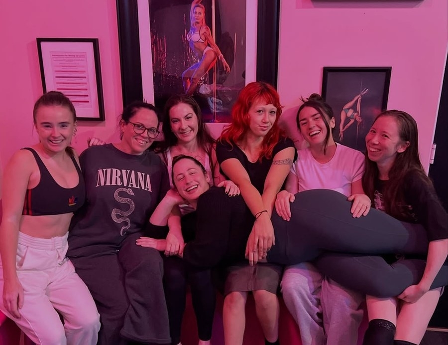A group of friends piled together laughing on a couch in a pink lit studio