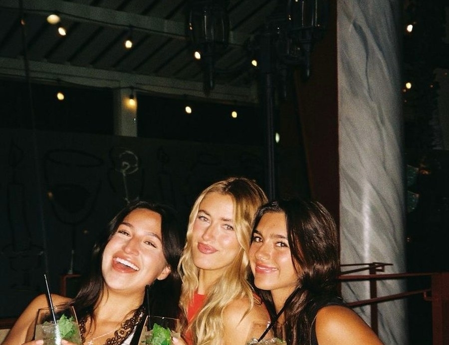 Three friends laughing together with cocktails at a bar at night