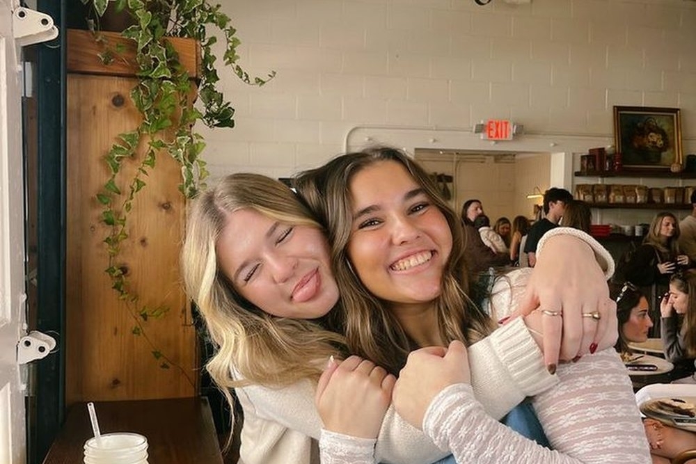 Two friends hugging and smiling at a busy cafe