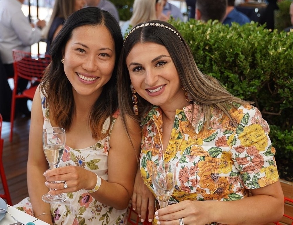 Two friends in floral dresses smiling with glasses of bubbly at a candlelit table
