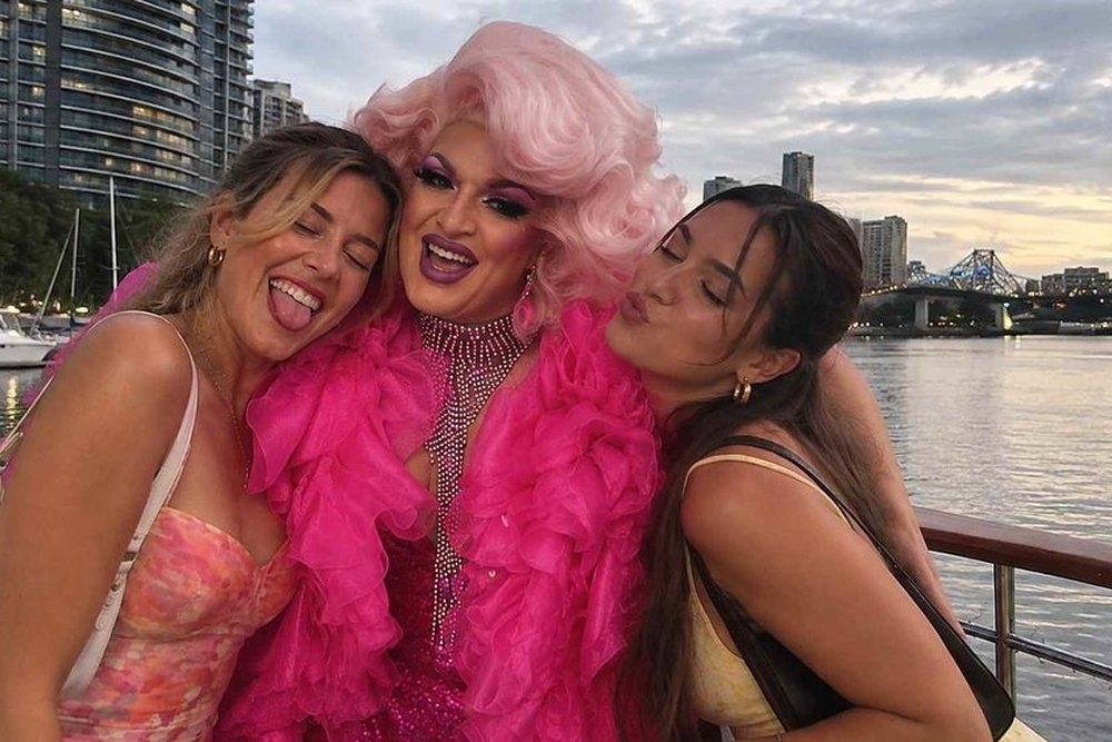 Two friends cuddling up to a drag queen in pink by the water