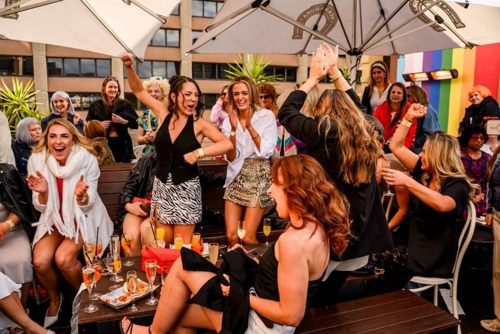 The girls up on their feet cheering and dancing at a rooftop drag brunch