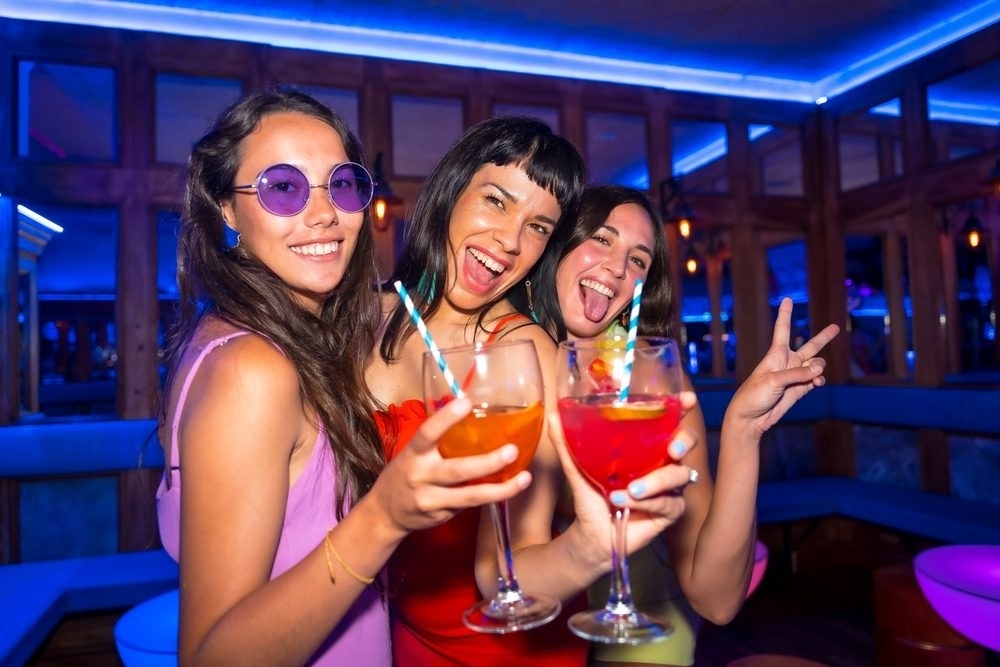 Three friends raising bright cocktails under blue lights at night