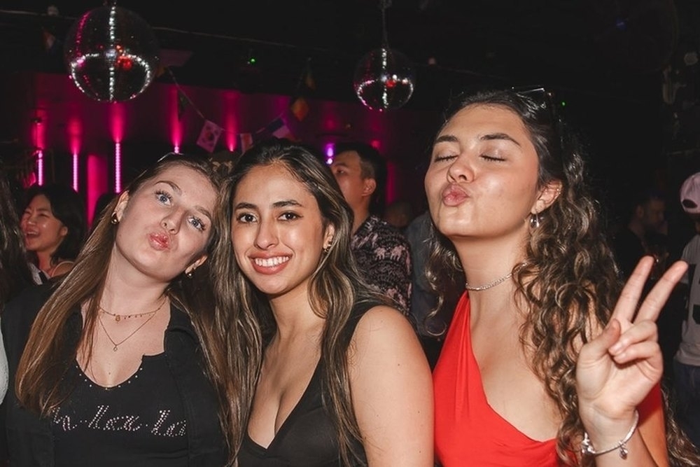 Three friends pouting and throwing peace signs at a busy bar