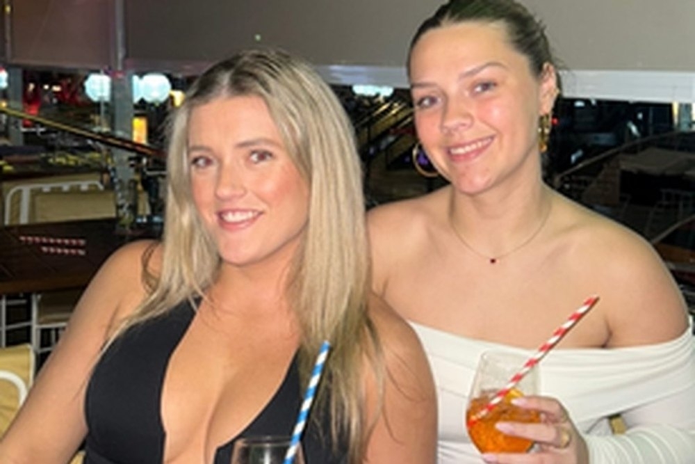 Two friends smiling with spritzes by the water
