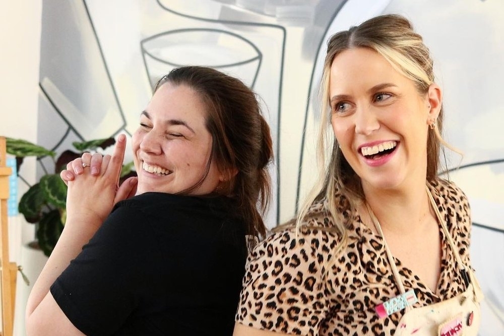 Two friends in paint splattered aprons laughing together at a painting class