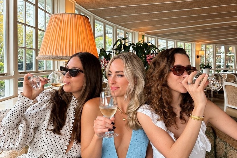 Three friends in sunglasses laughing on a banquette at brunch