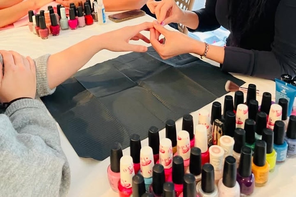 A manicurist painting nails at the table with polish lined up