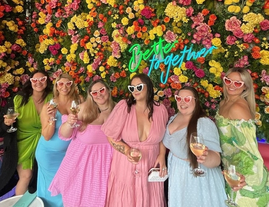 The girls in heart sunglasses posing in front of a flower wall at lunch