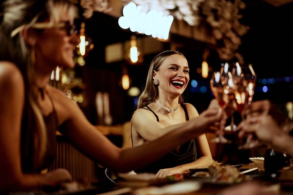 Two friends laughing and clinking sparkling wine at a candlelit bar