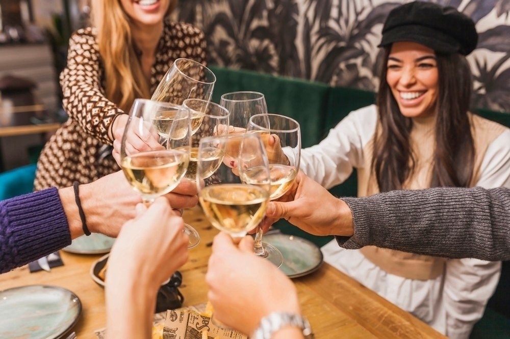 Friends laughing as they clink glasses of white wine across the table