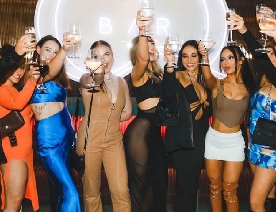 A group of friends in going-out outfits raising their glasses under a big round light