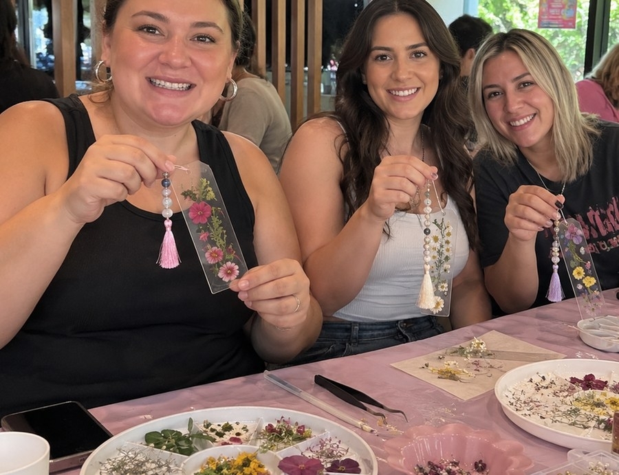 Three friends proudly holding up the bookmarks they made at a craft workshop