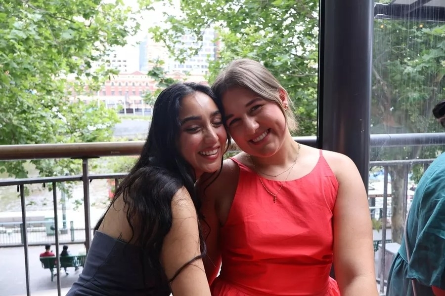 Two friends cheek to cheek by the river with leafy trees behind