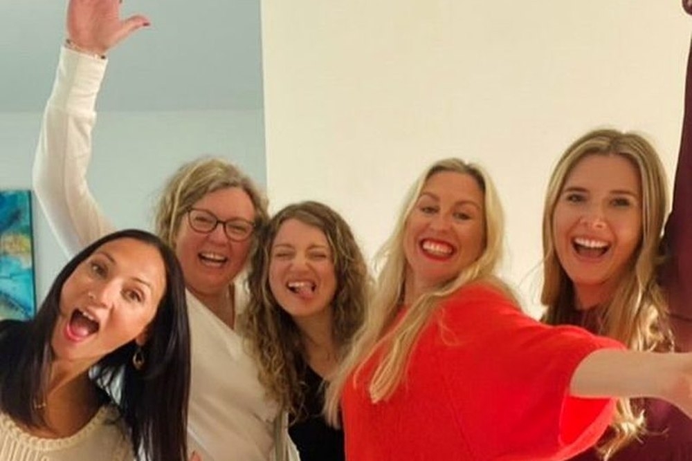 The girls cheering and waving for a group selfie back at the apartment