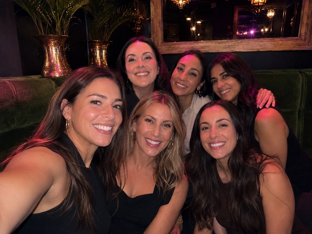 Six friends squeezed into a close group selfie at a warm and lively bar