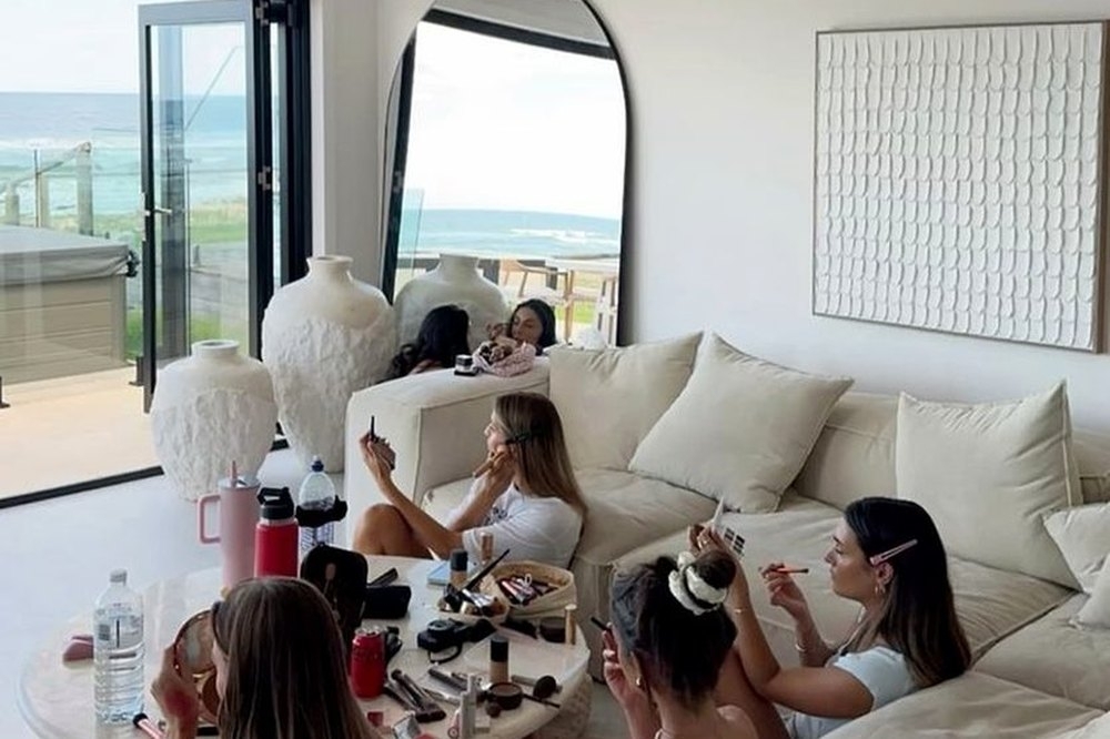 Friends doing their makeup together on big white sofas before heading out